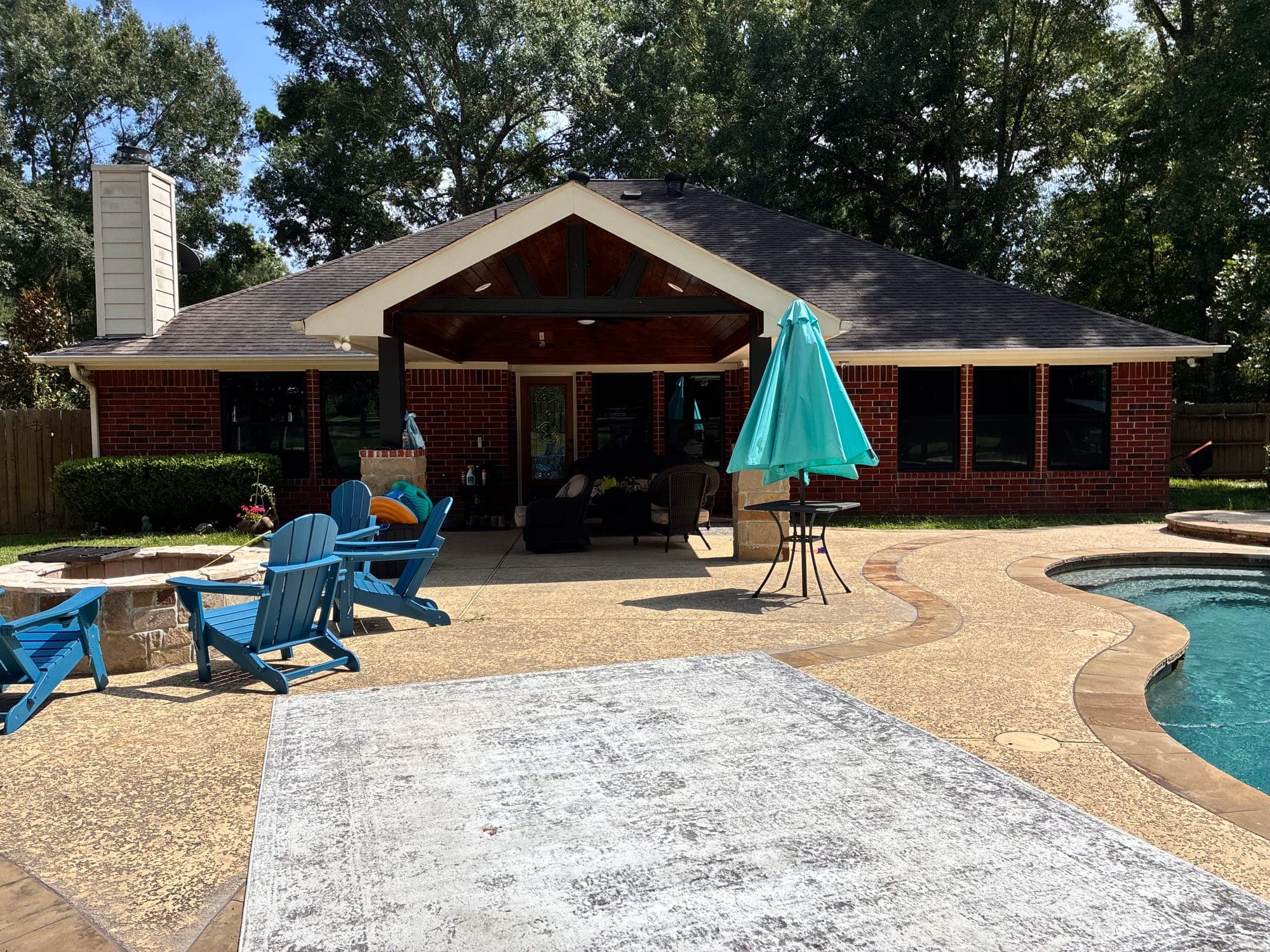 Red-brick pool house with black-framed picture windows beside a covered patio