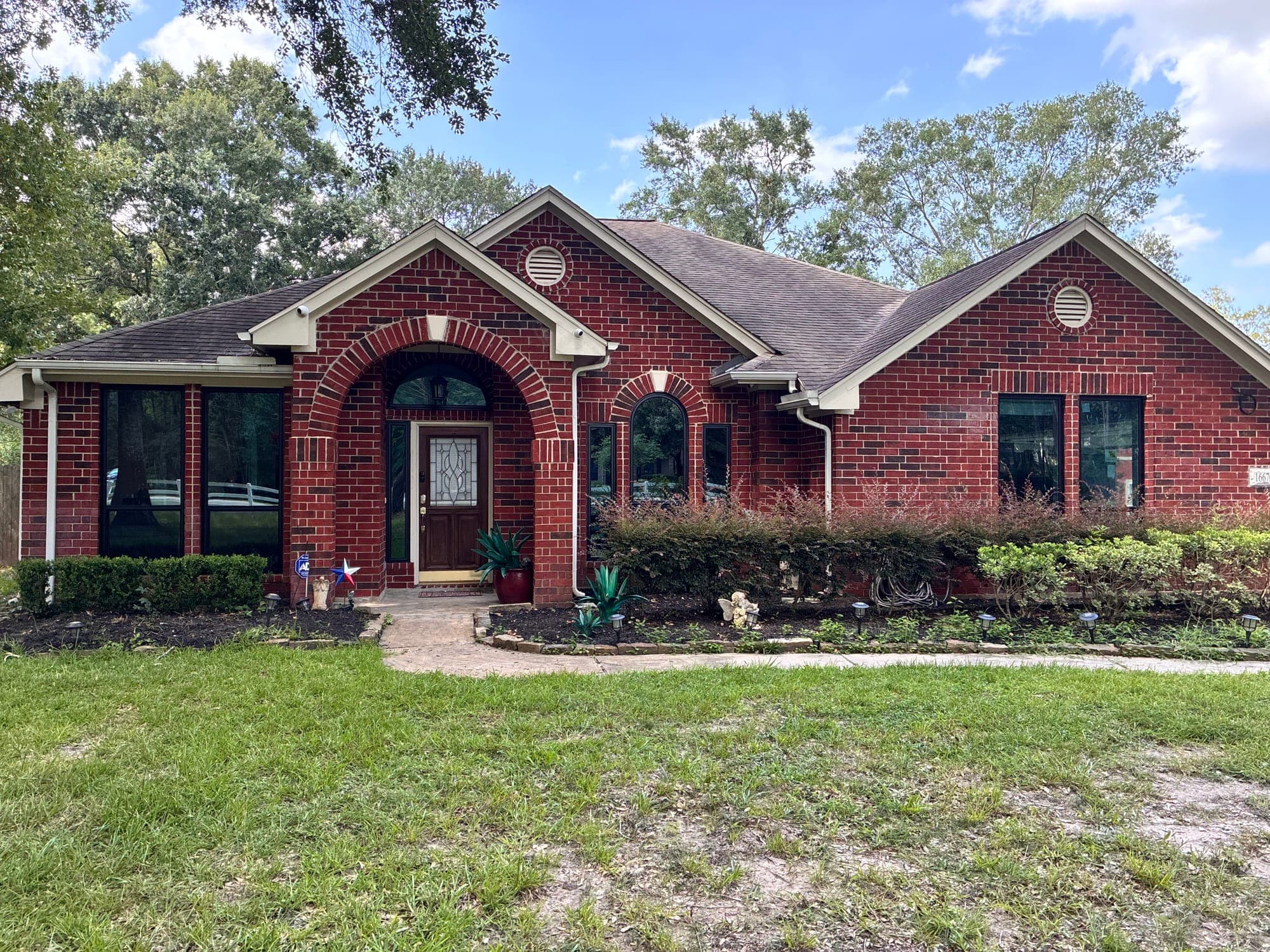 Red-brick ranch home with black-framed picture windows and an arch-top accent