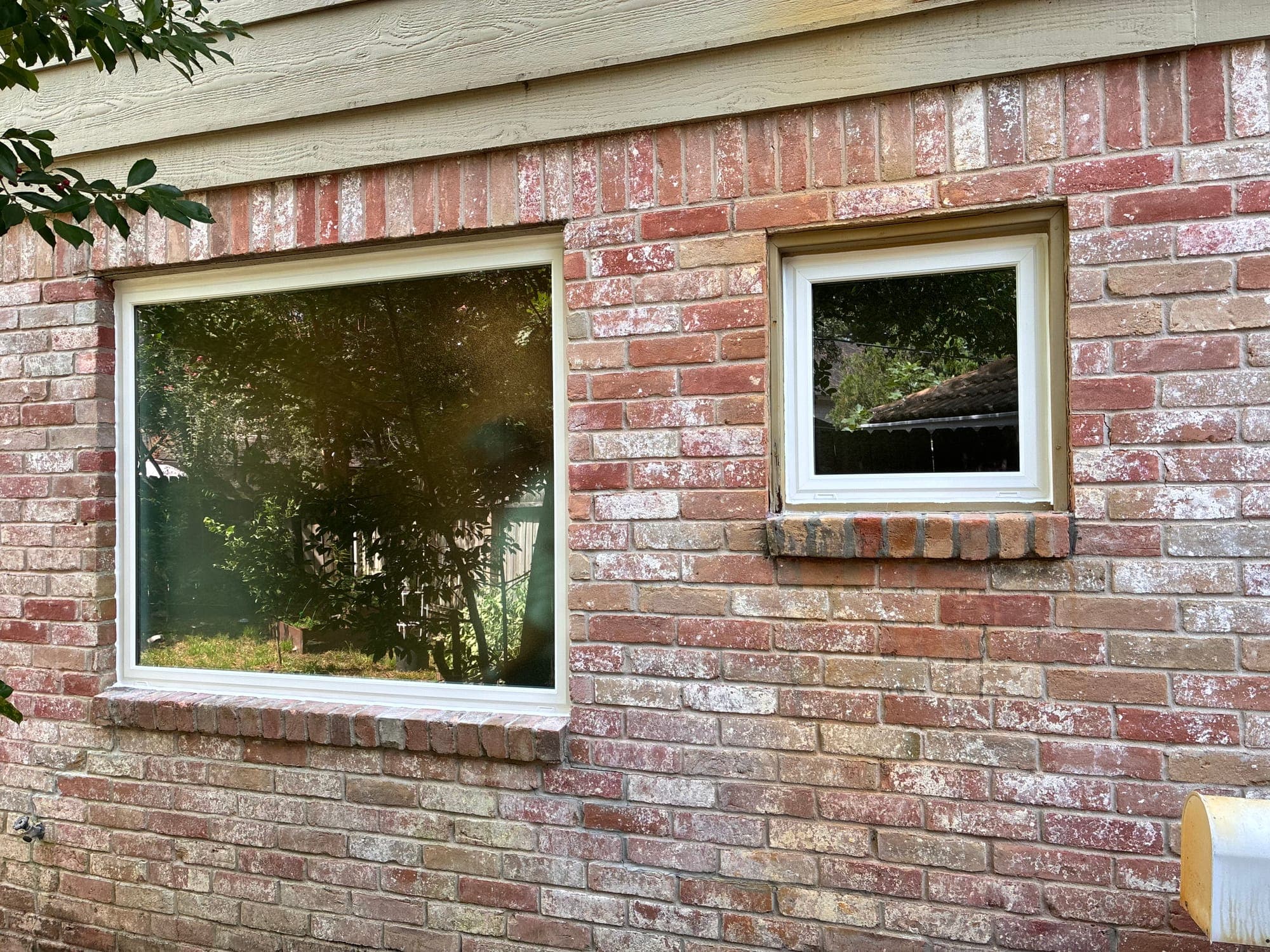 A wide white-framed picture window beside a smaller unit on antique blush brick