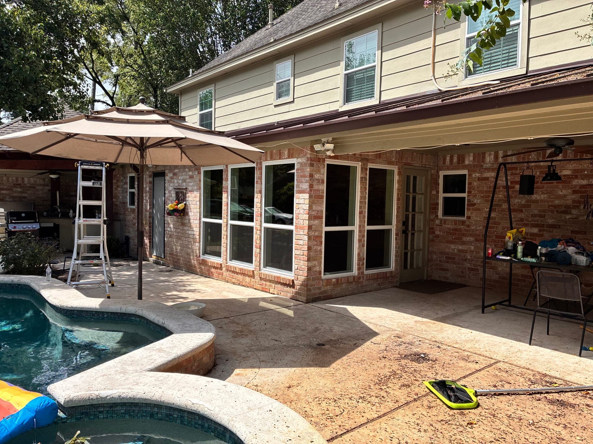 White-framed picture windows wrapping a brick corner beside a backyard pool