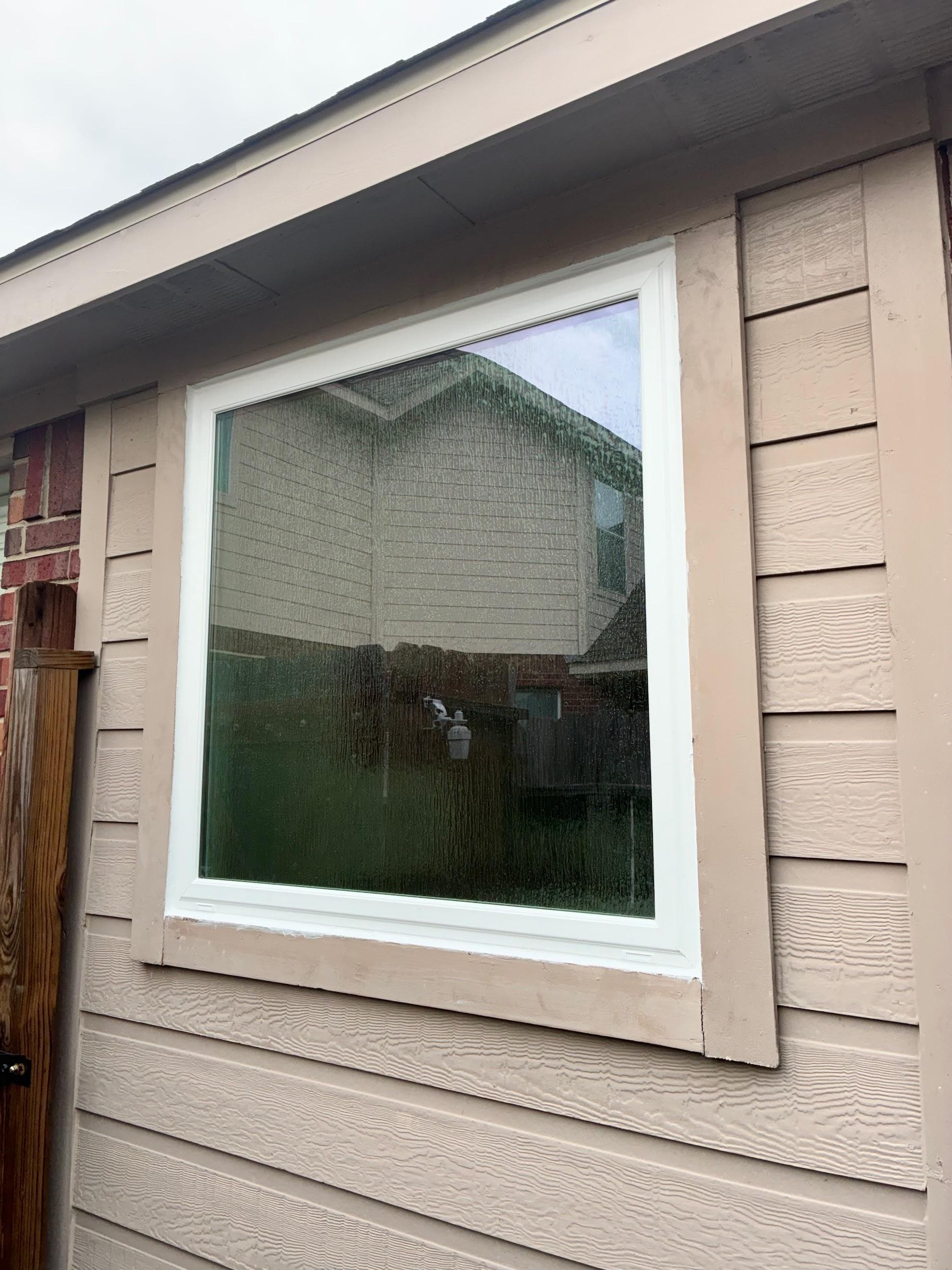 A single white-framed picture window on tan lap siding