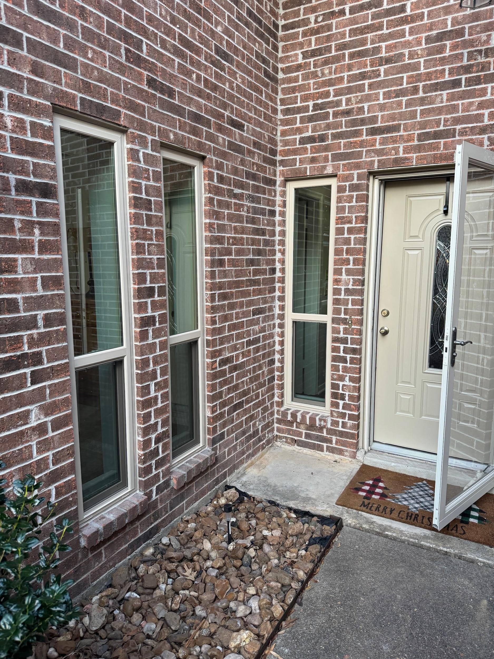 Two almond-framed single-hung windows beside a white entry door on red brick