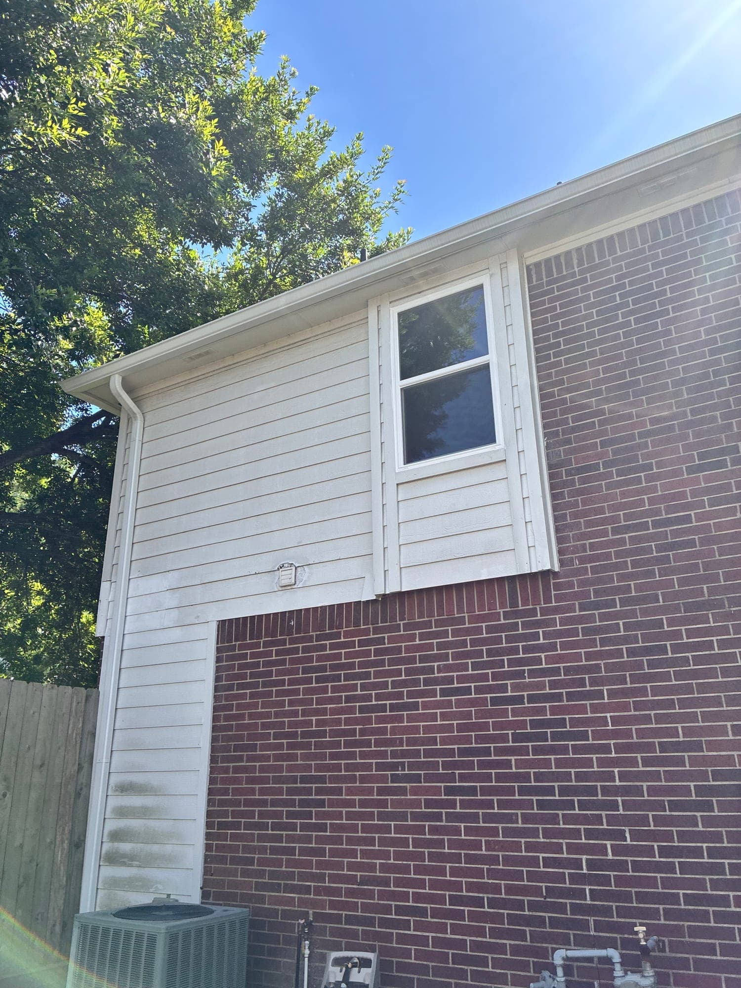 A white single-hung window set into white siding above dark brick