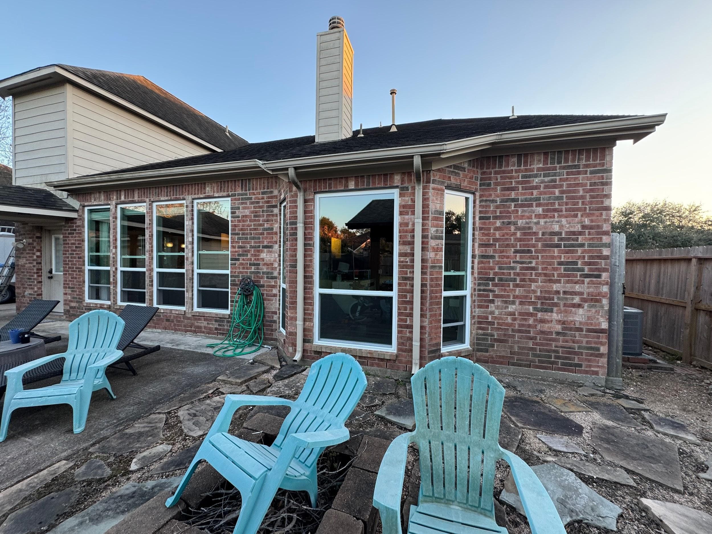 White-framed sliding and picture windows across a brick backyard elevation with a patio