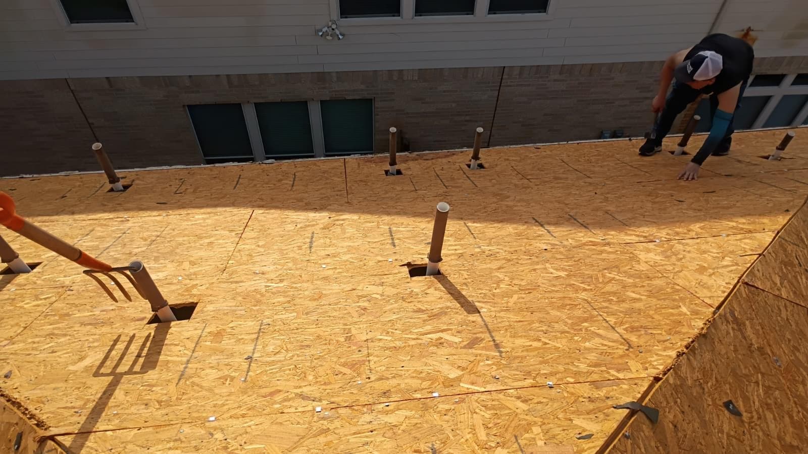 Crew member nailing new OSB decking on a large sunlit roof slope